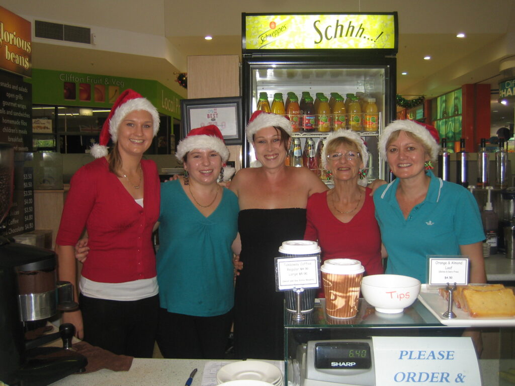 Smiling café team wearing Santa hats behind the counter at Glorious Beans café, celebrating Christmas in 2011.