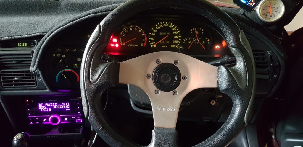 Close-up view of a sporty car steering wheel and illuminated dashboard gauges, symbolizing control and focus.