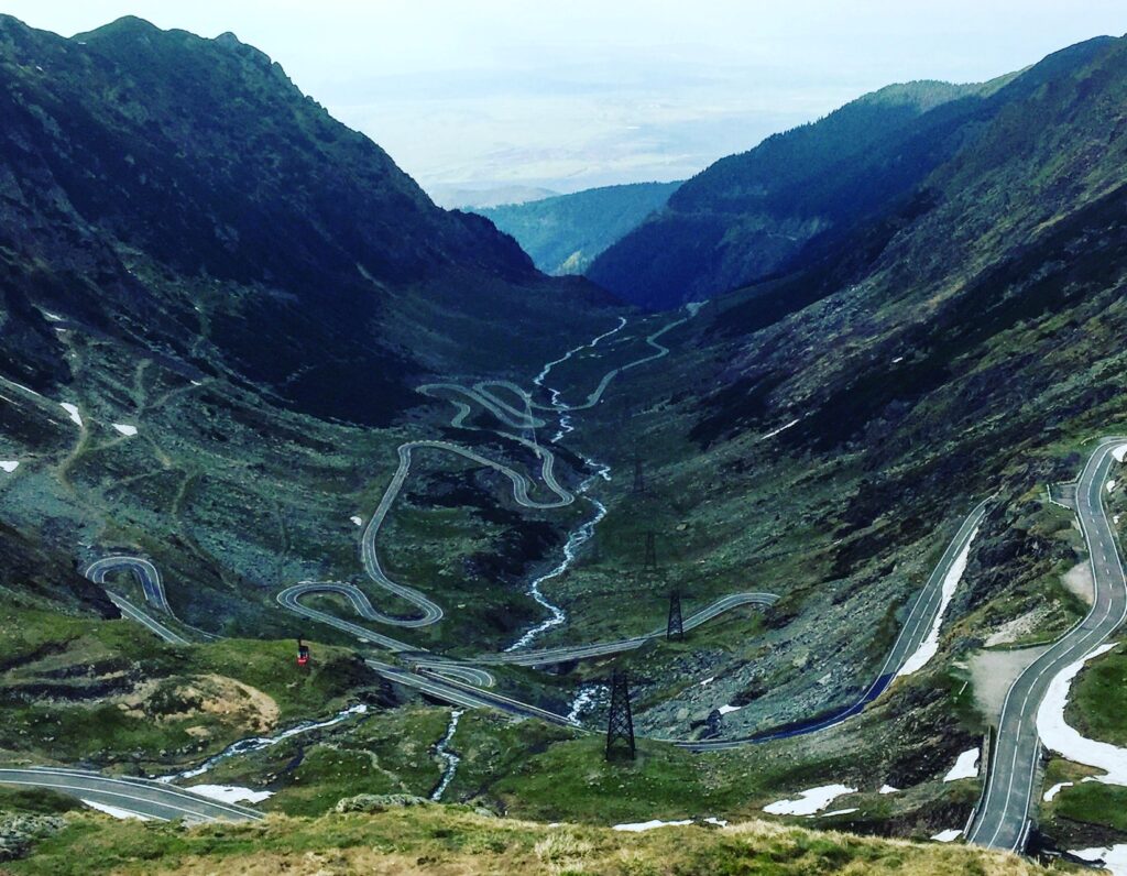 A winding mountain road with sharp hairpin turns cutting through a steep green valley, symbolizing the challenging path to success.