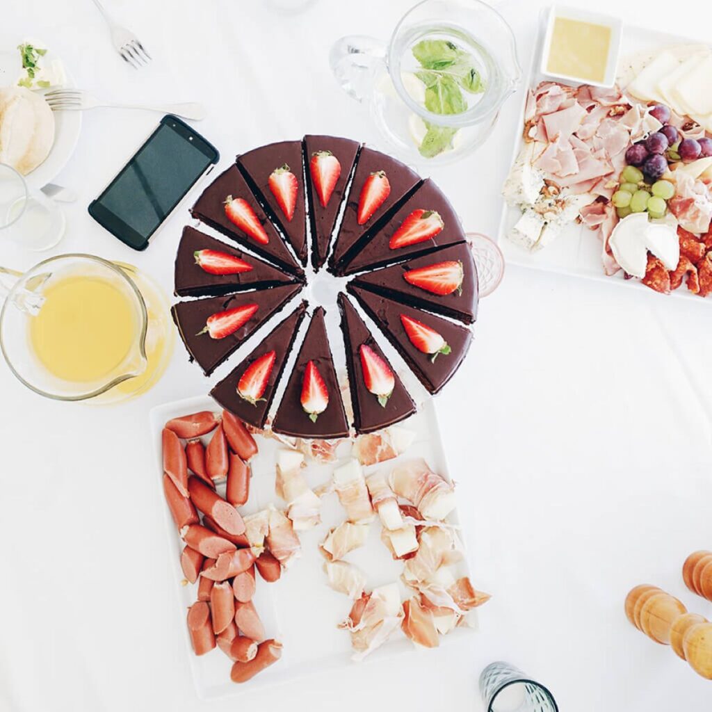 Overhead view of a café table with sliced chocolate cake, brunch platters, and drinks, showcasing menu variety and presentation