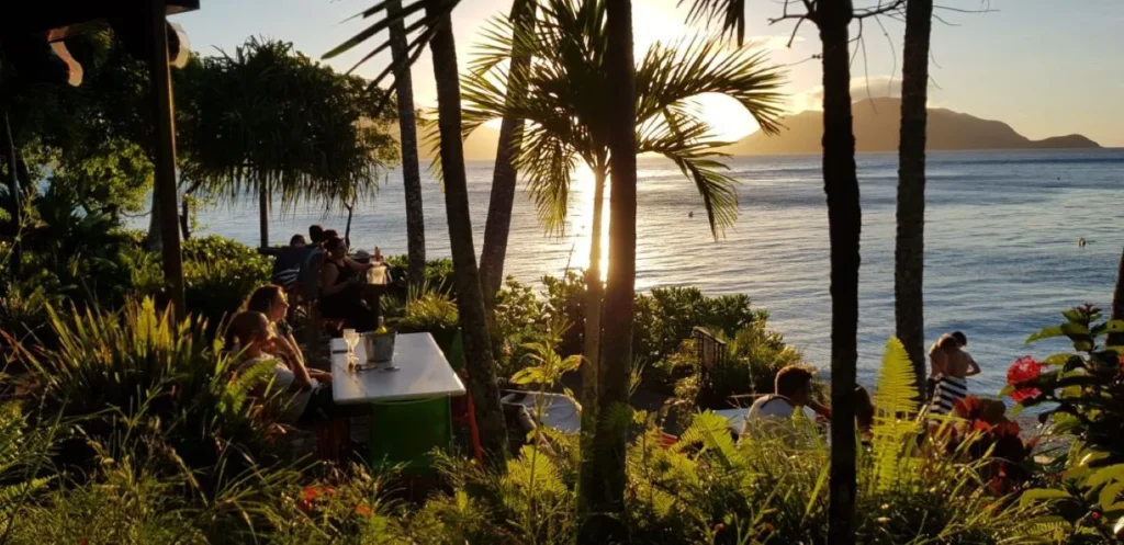 Customers enjoying a tropical beachfront café setting at sunset, highlighting the atmosphere and experience hospitality venues create